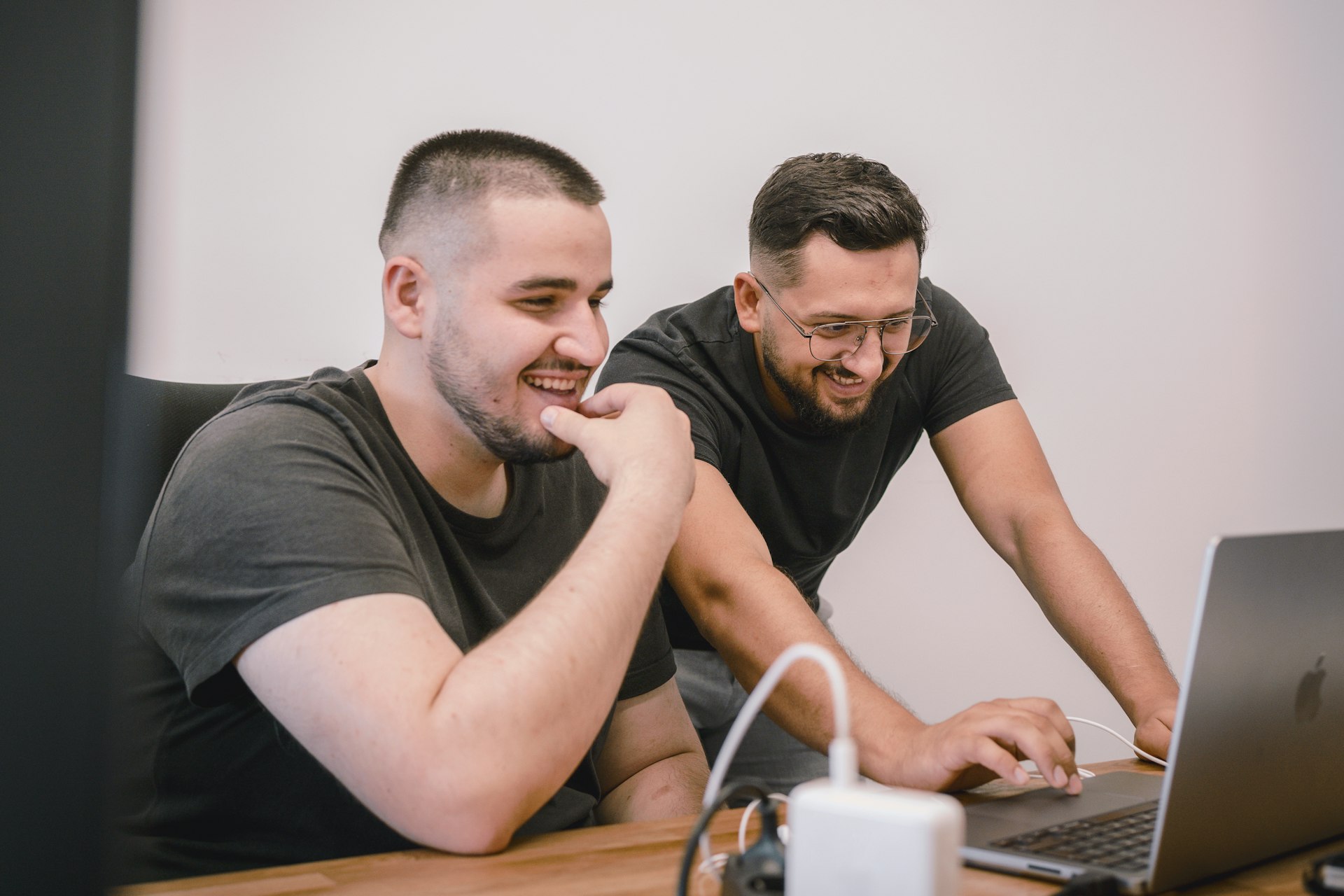 two men sitting at a table looking at a laptop